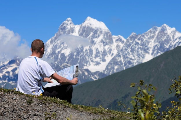 Trekking in the mountains. Tourist checks the route with the map. View of the peak of Ushba. Main Caucasian ridge, Zemo Svaneti, Georgia. World beauty