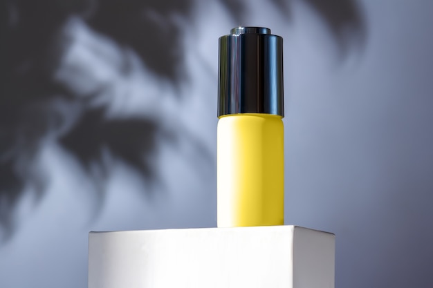 Trendy 2021 year Ultimate Gray and Illuminating colors. Stylish composition with a yellow dropper bottle on a stand on a gray wall with the shadow of the leaves.