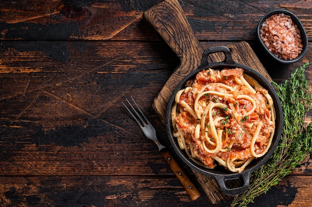 Trendy baked Feta pasta with Oven roasted tomatoes and cheese in a pan. Dark wooden background. Top view. Copy space.