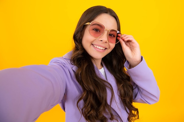 Trendy beautiful teenage model making selfie posing on yellow studio background Teen fashion