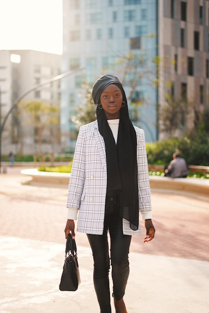 Trendy black woman in headscarf carrying bag in park