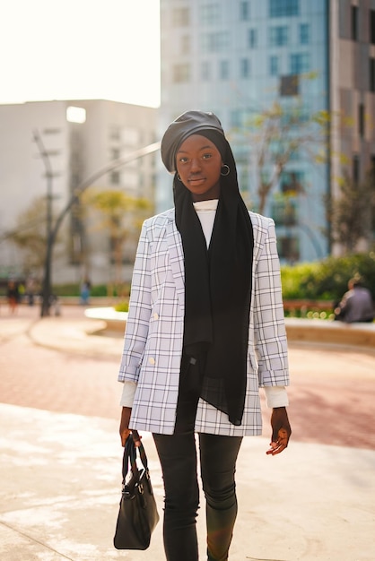 Trendy black woman in headscarf carrying bag in park