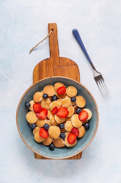 Trendy breakfast with mini pancakes, blueberries and strawberries, top view.