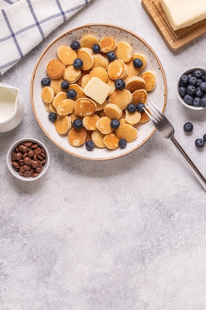 Trendy breakfast with mini pancakes and blueberries, top view.