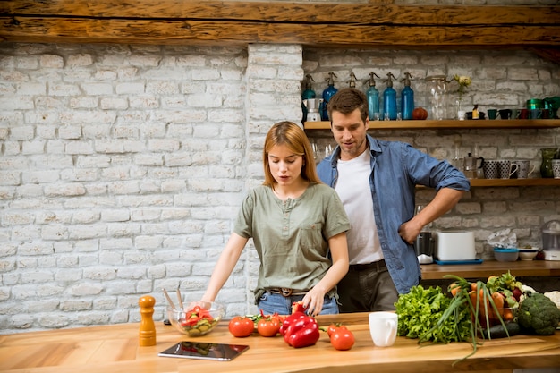 Trendy couple peeling and cutting vegetables from the market in rustic kitchen