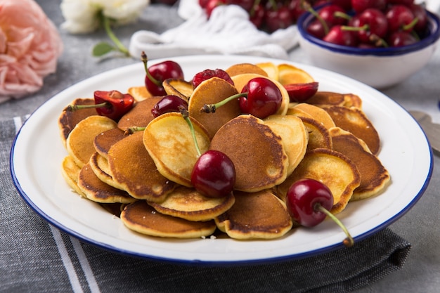 Photo trendy food, mini cereal pancakes with cherry in bowl on the table