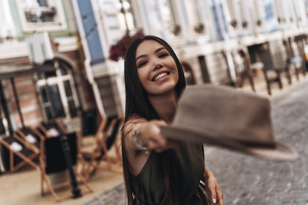 Trendy girl. Attractive young woman throwing a hat and smiling while standing outdoors