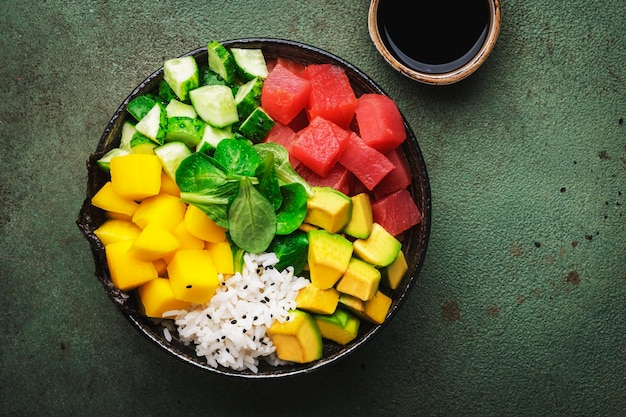 Trendy hawaiian poke bowl with tuna avocado mango cucumber lamb lettuce and white rice Soy sauce and sesame dressing Old green table background top view