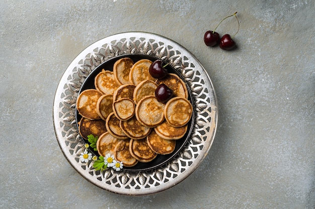 A trendy homemade breakfast with tiny pancakes close-up. Mini pancakes, cherries, tea on the table in an openwork plate. Horizontal orientation