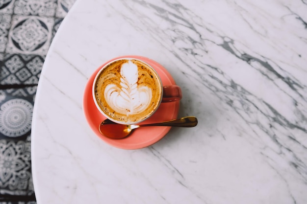 Trendy pink cup of hot cappuccino on marble table background beautiful latte art on the top