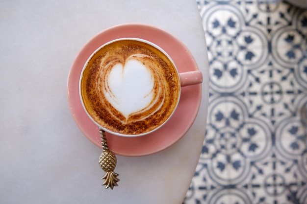 Trendy pink cup of hot cappuccino on marble table background Heart shape latte art for symbol of love One cup for morning routine