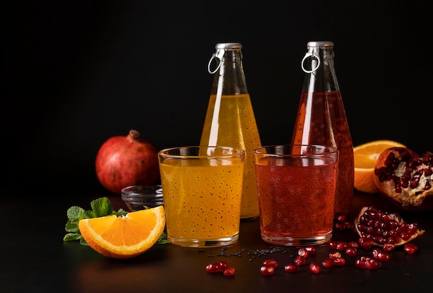 Trendy pomegranate and orange drink with basil seeds in bottles on black background. Closeup