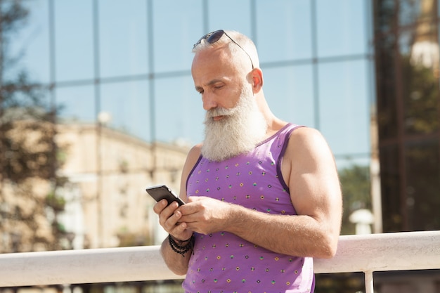 Trendy senior man using smartphone in downtown center outdoor - Mature fashion male having fun with new trends technology - Tech and joyful elderly lifestyle concept