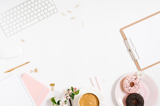 Trendy stylish frame for a female blogger freelancer notebooks tablet keyboard donut on a plate apple blossoms on a white background with a place to copy