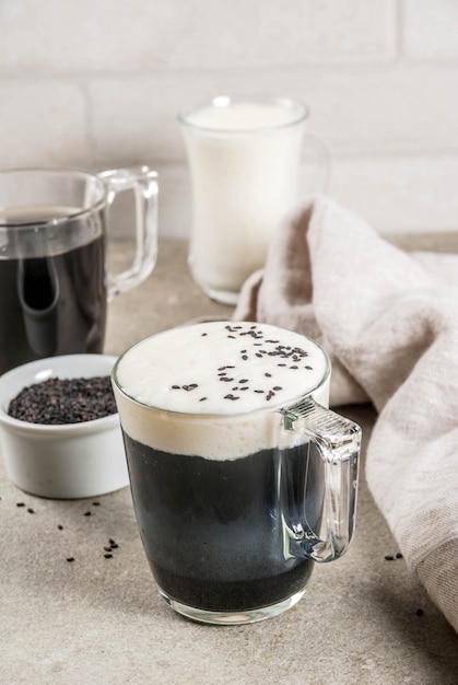 Photo trendy vegan food recipes, black sesame cappuccino with sesame seeds and whipped coconut milk, grey stone table,  copyspace