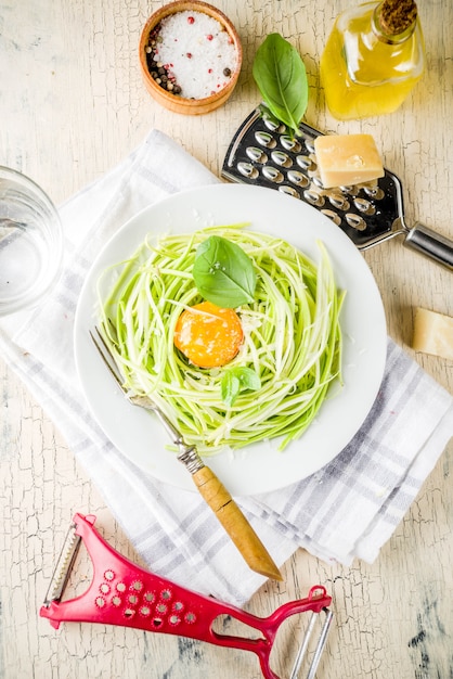 Photo trendy vegan food recipes, cheese zucchini spaghetti pasta with egg yolk with parmesan, olive oil and basil leaves, light concrete surface