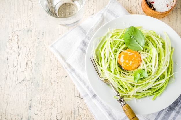 Trendy vegan food recipes, cheese zucchini spaghetti pasta with egg yolk with parmesan, olive oil and basil leaves, light concrete table