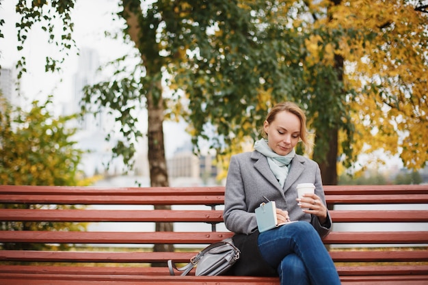 Trendy woman in stylish coat sitting on the bench in city park