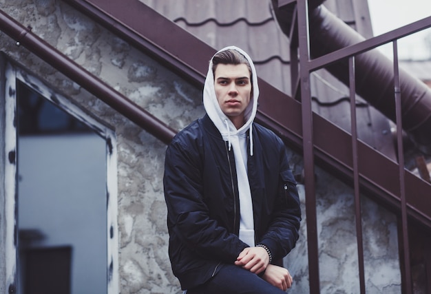 Trendy young man in black jacket posing in street