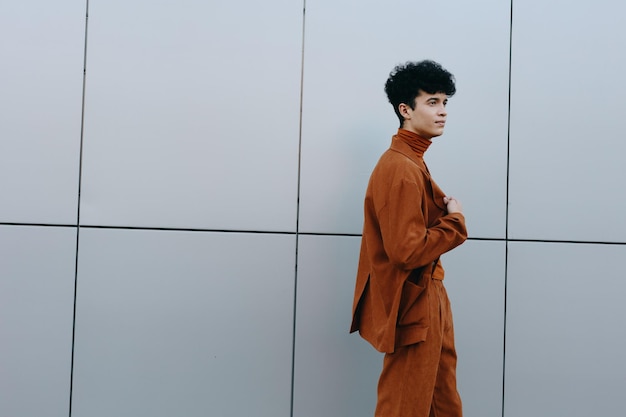 Trendy young man in an orange outfit standing against a modern gray wall