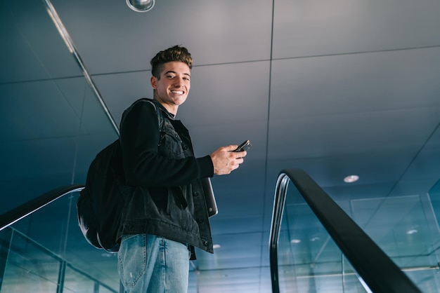 Trendy young man with phone on moving stairs