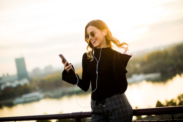 Trendy young woman listening music from smartphone outdoor at sunset