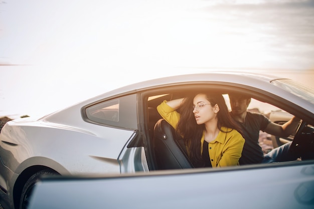 Trendy young women and man traveling by car. Relaxed happy couple on summer roadtrip travel vacation.