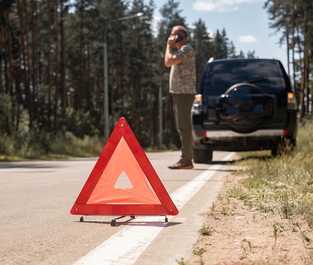 Triangle caution sign on road after car breakdown and driver talking on phone waiting for emergency ...