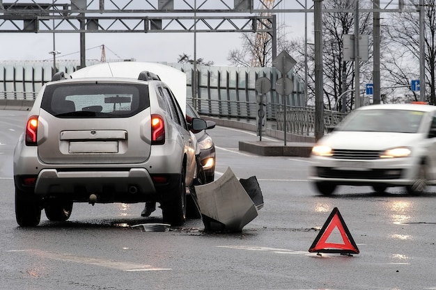 Triangular red retro-reflective sign of accident on the road. Collision of two cars. Broken bumper and hood. Car accident on the street.