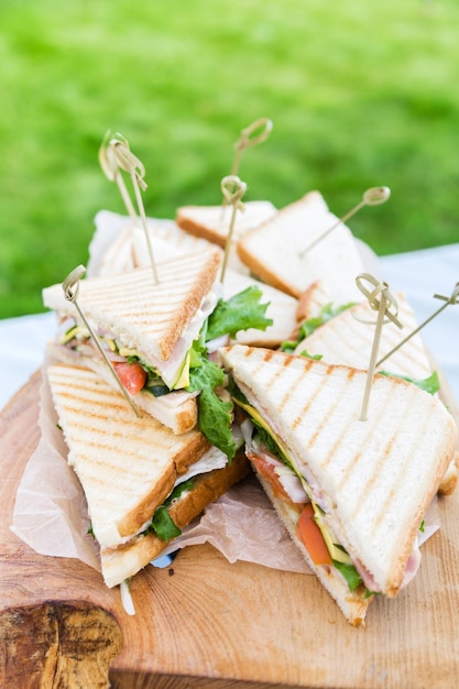 Triangular shaped sandwich with ham vegetables and mayonnaise on a wooden platter Menu for an outdoor event in summer Horizontal photo