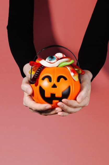 Trick or treat. Pumpkin Jack filled with various creepy sweets stands on stones and moss. Woman hand holds basket