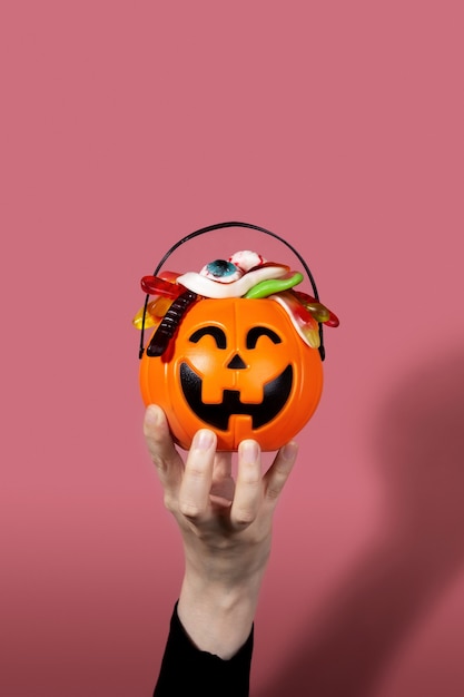 Trick or treat. Pumpkin Jack filled with various creepy sweets stands on stones and moss. Woman hand holds basket