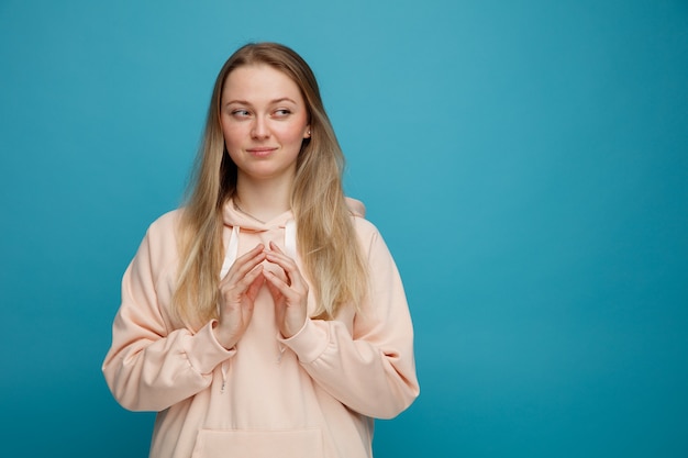 Tricky young blonde woman keeping hands together looking at side 