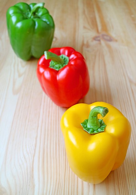 Tricolor Bell Peppers Lined Up on Light Brown Wooden Background