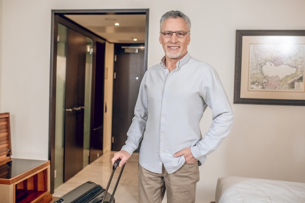 Trip. Gray-haired confident man with a suitcase in a hotel room