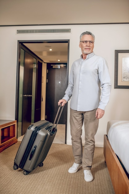 Trip. Gray-haired confident man with a suitcase in a hotel room