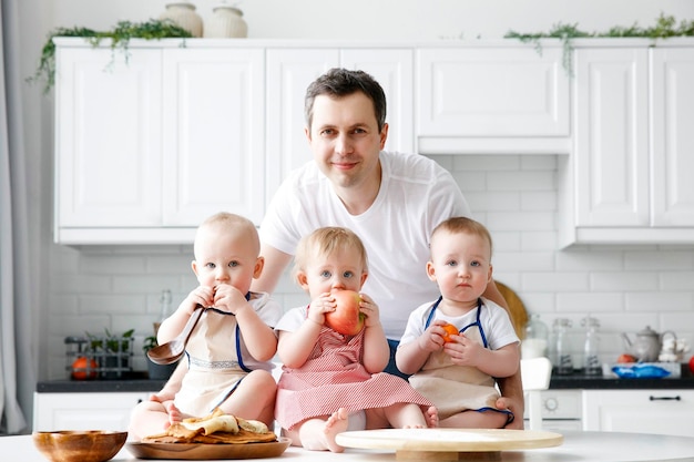 Triplets two boys and a girl in the arms of a happy father kitchen background