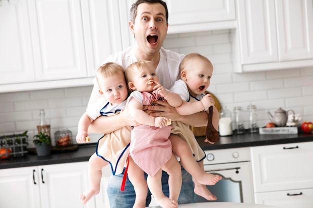 Triplets two boys and a girl in the arms of a happy father kitchen background