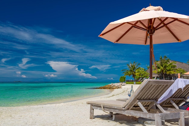 Tropical beach background as summer landscape with lounge chairs bed umbrella, calm sea sand sky