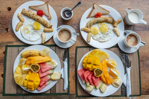 Tropical breakfast of fruit coffee and scrambled eggs and banana pancake for two on the beach near sea Top view table setting