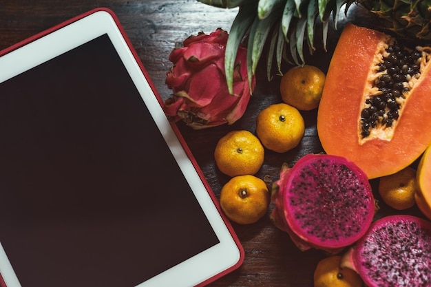 Tropical fruit near modern laptop on wooden background Vegan lifestyle