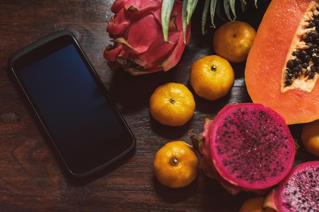 Tropical fruit near modern phone on wooden background Vegan lifestyle