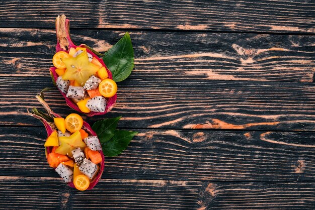 Tropical Fruit Salad Served in half a Dragon Fruit. Papaya, rambutan, tamarind, cactus fruit, mango. On a wooden background. Top view.