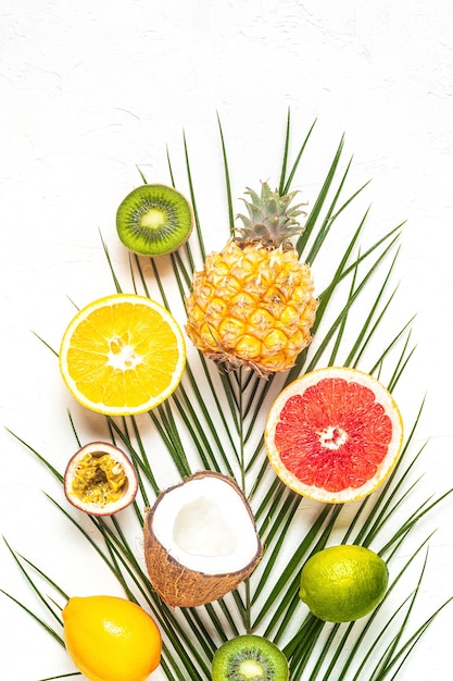 Tropical fruits and palm leaves on a white background, top view.