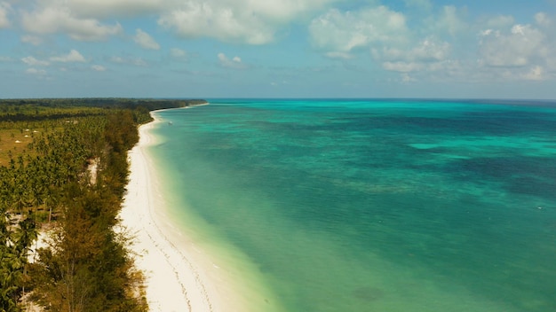 Tropical island with sandy beach by atoll with coral reef and blue sea