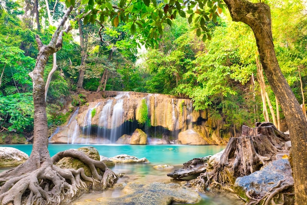 Tropical landscape with beautiful waterfall emerald lake rocks and large tree roots in wild jungle forest Erawan National park Kanchanaburi Thailand