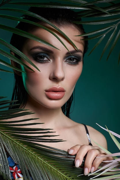 Tropical portrait sexy woman in leaves palm tree. Bright green makeup, shadow of palm leaves on girl face. Beautiful makeup