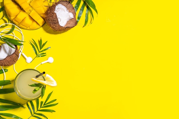 Tropical summer background with hat mango coconut tropical fruits palm leaves headphones Summer holiday vacation flatlay leisure travel concept Top view copy space for text