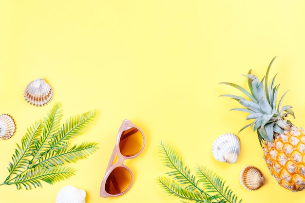 Tropical summer concept with woman fashion accessories, leaves and pineapple on yellow background. Flat lay, top view