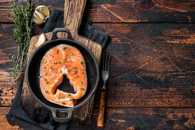 Trout or Salmon raw steaks in a pan with thyme. Dark wooden background. Top view. Copy space.